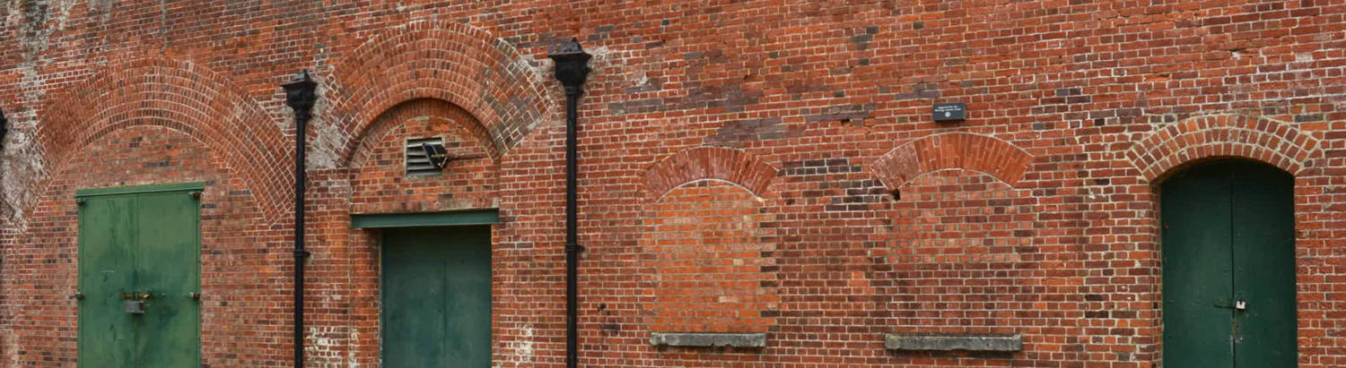 Hilsea Lines. Red brick military building with three green doors with brick arches above and two bricked up windows 